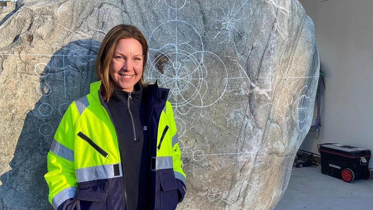 Bilde av en kvinne i arbeidsantrekk foran en steinskulptur